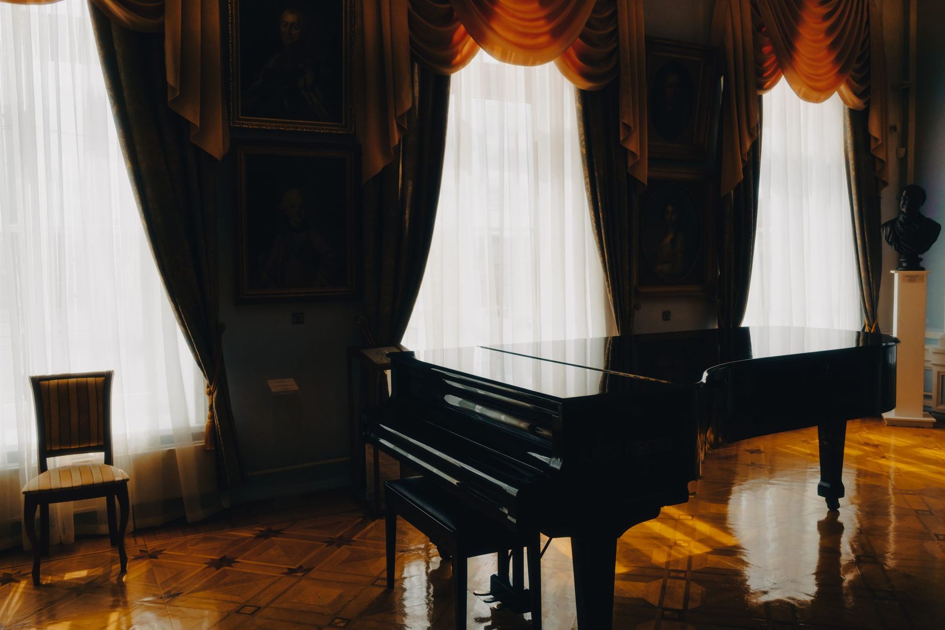 A black grand piano in a sunlit room with tall curtained windows