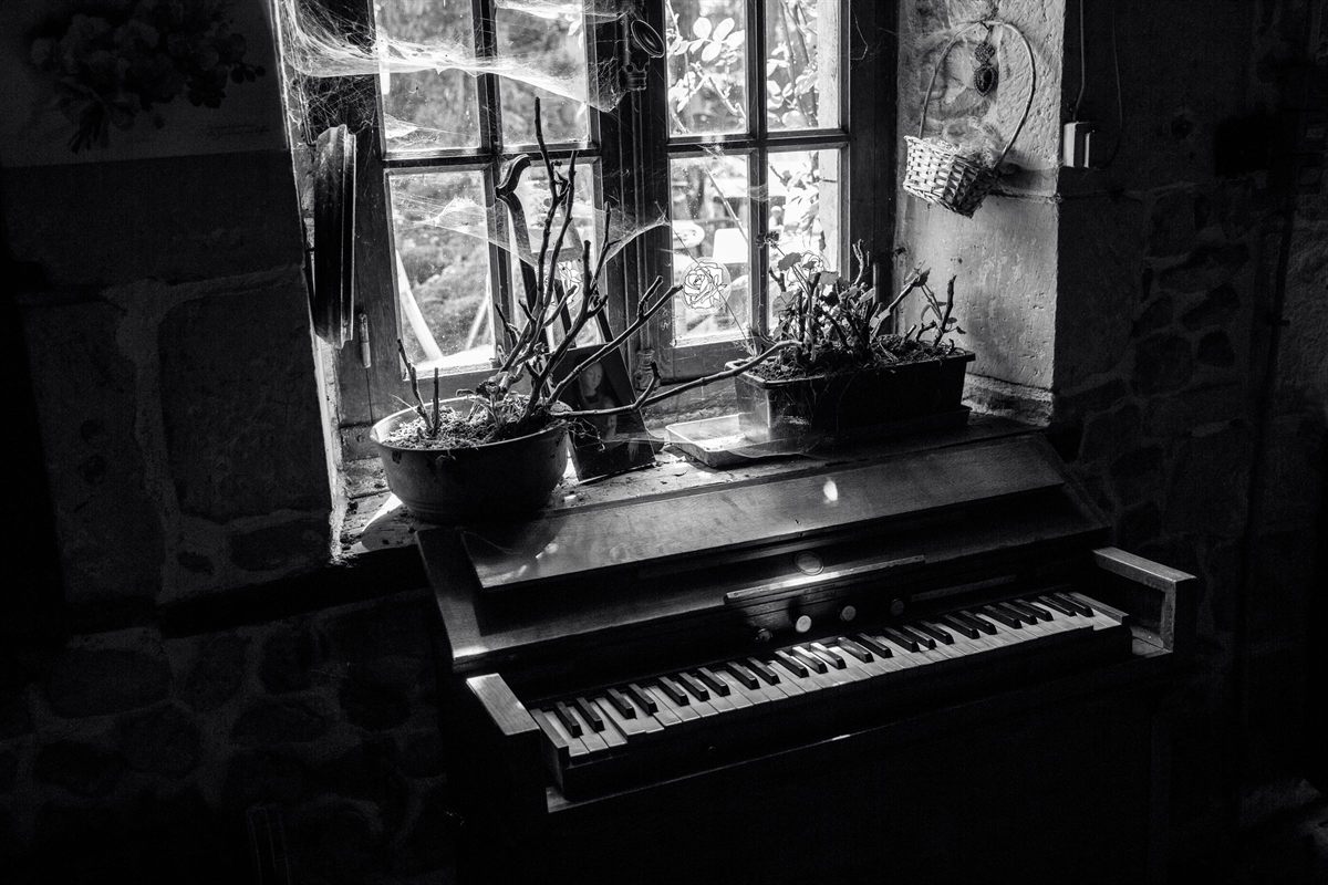 A vintage upright piano beneath a window, in black and white