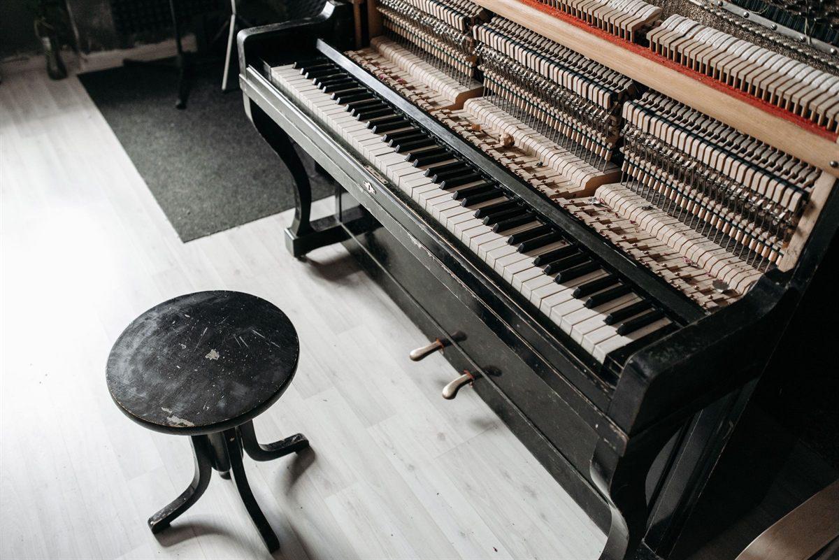 An open upright piano showing its strings, with a stool beside it