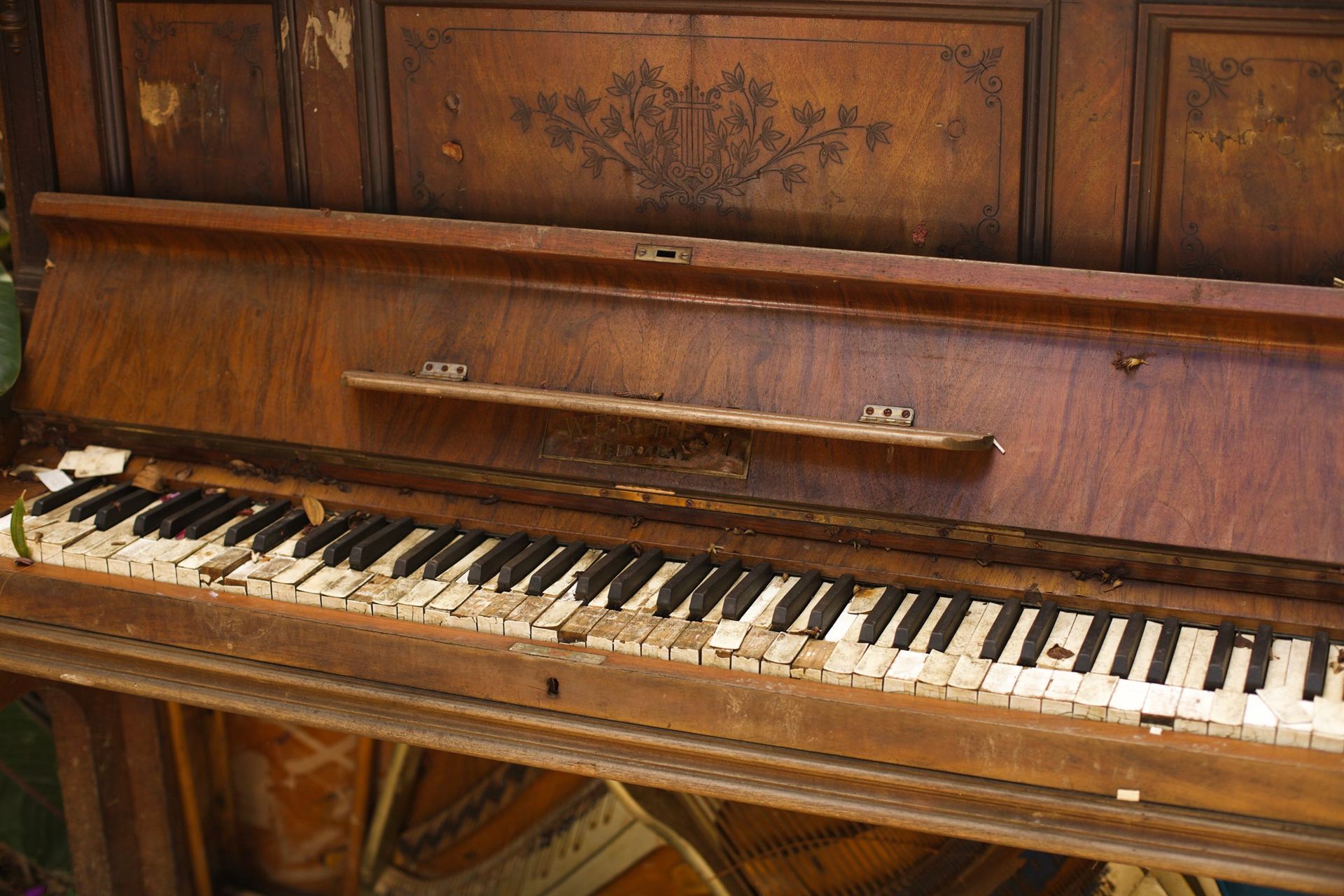An old timber upright piano with worn keys and a carved panel
